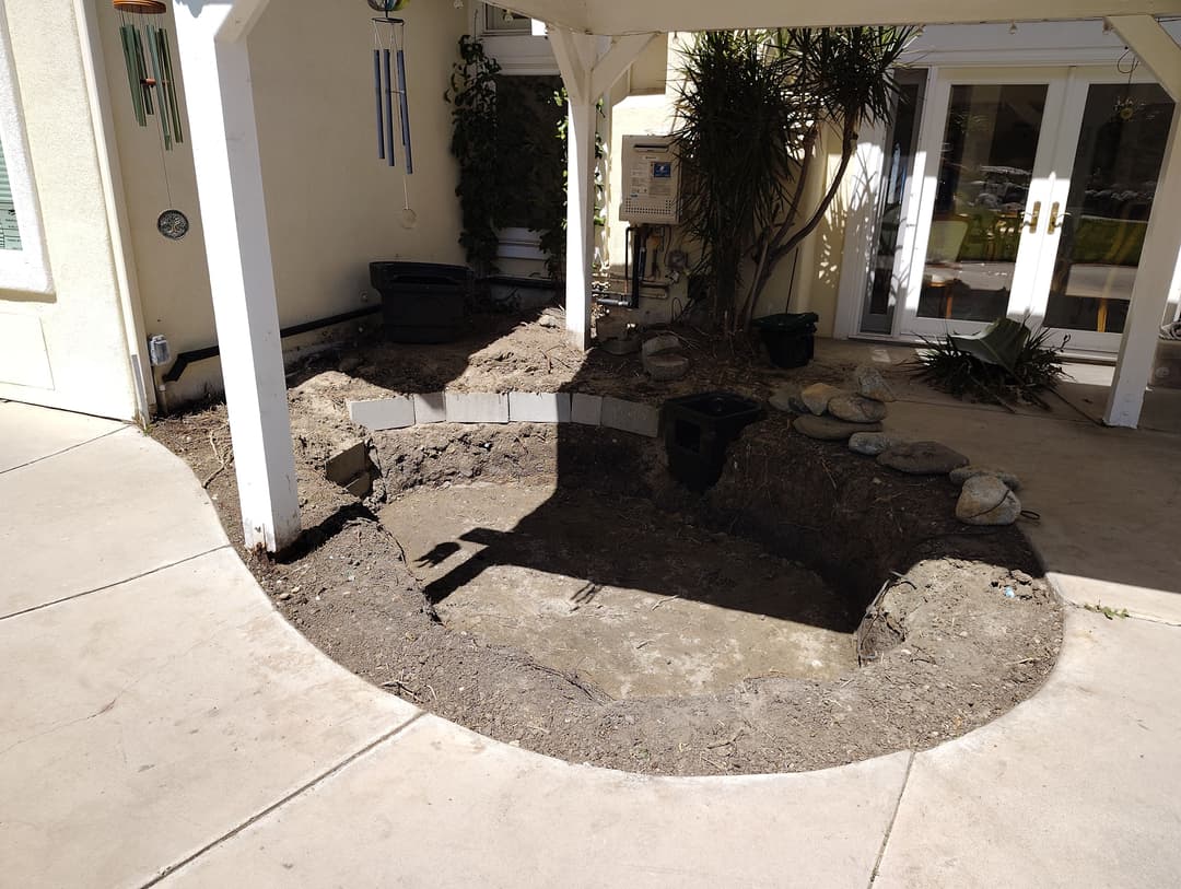 Excavated garden area with rocks, ready for landscaping near a house.