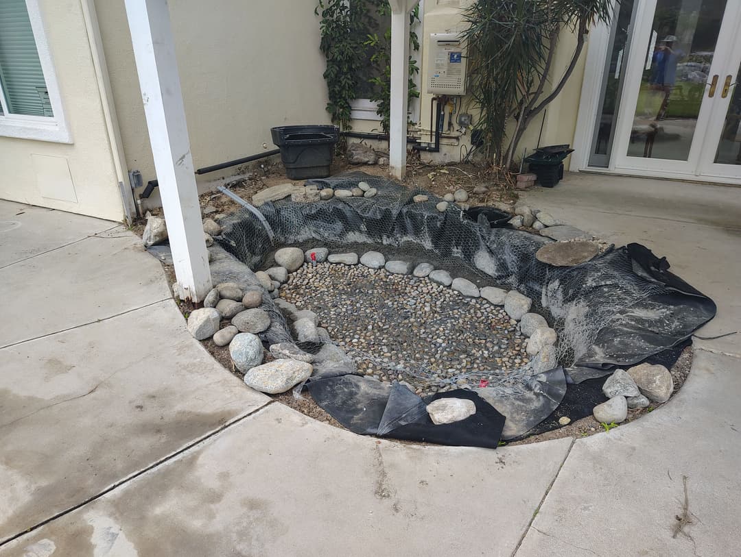 Landscape pond area with rocks, fabric liner, and surrounding concrete patio for outdoor design.