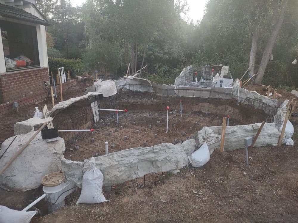 In-progress construction of a backyard pool with rebar and plumbing in place.