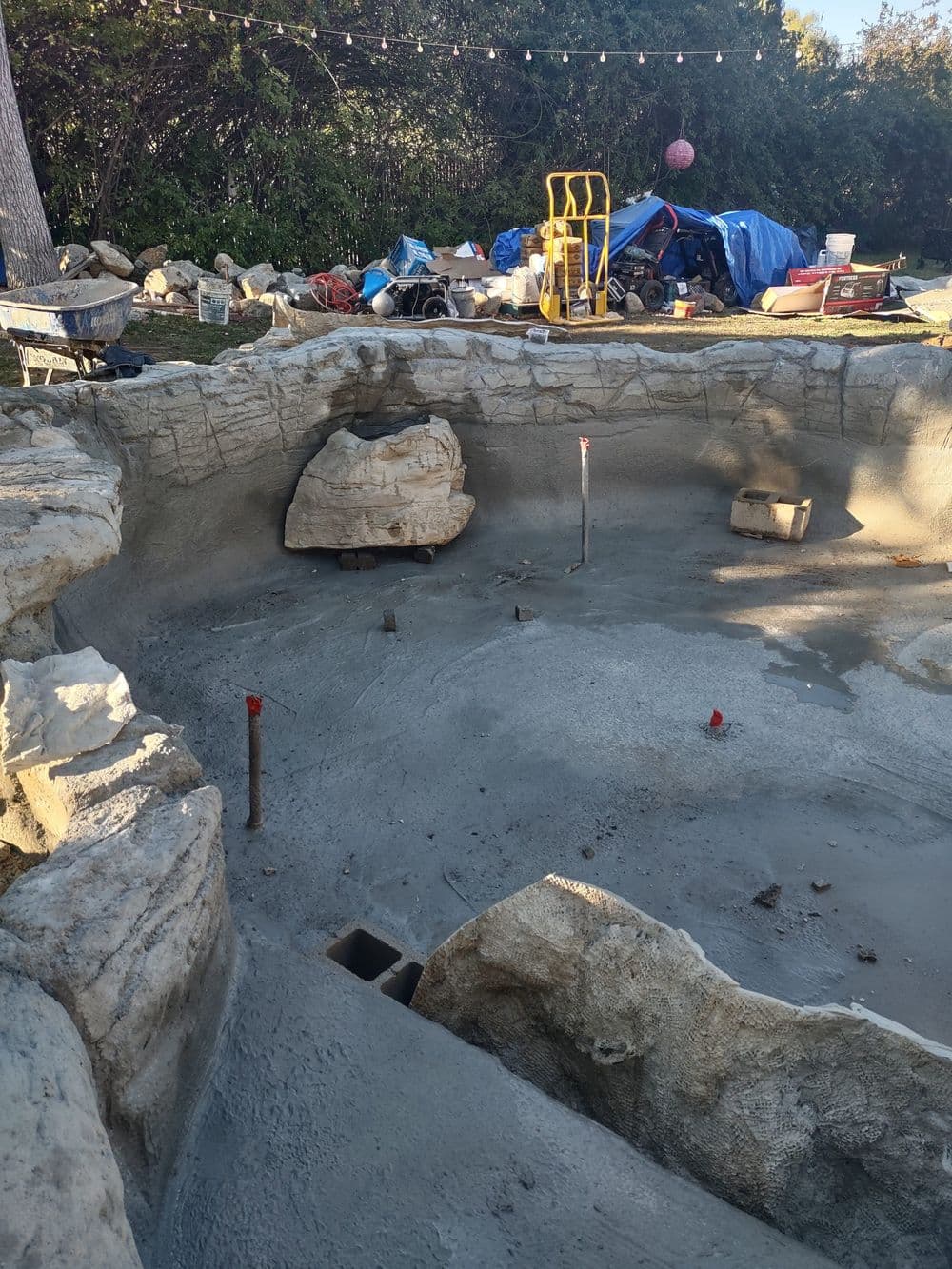 Construction site of a stone-lined pool, showing unfinished concrete and landscaping elements.