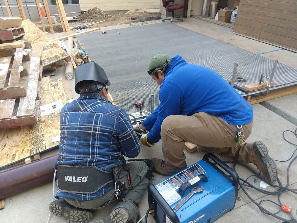 Two workers welding metal components on a construction site with tools and materials around them.
