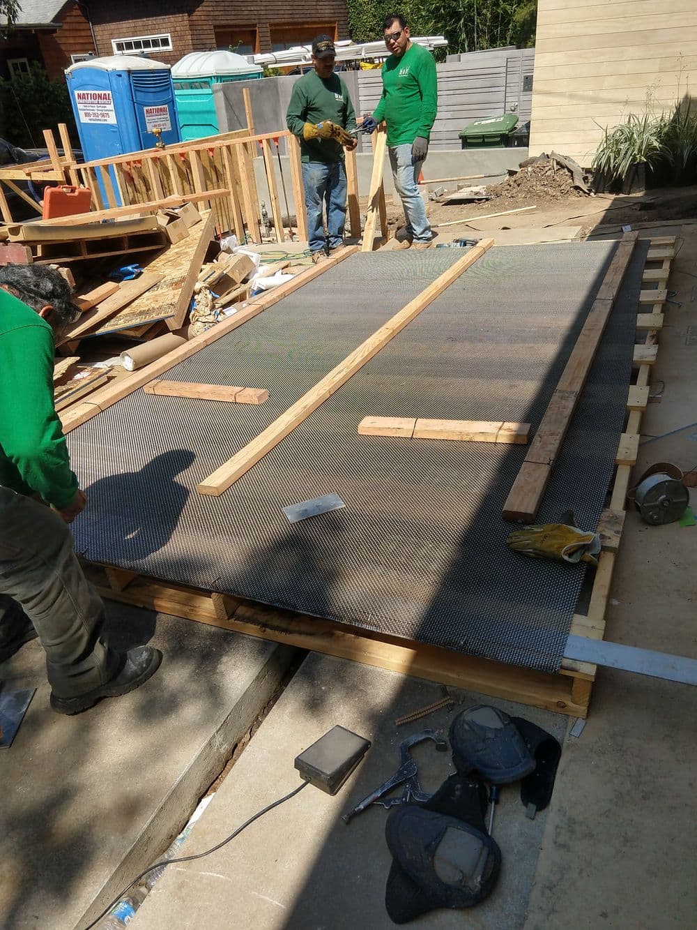 Construction workers installing a mesh foundation on a building site with wooden supports nearby.