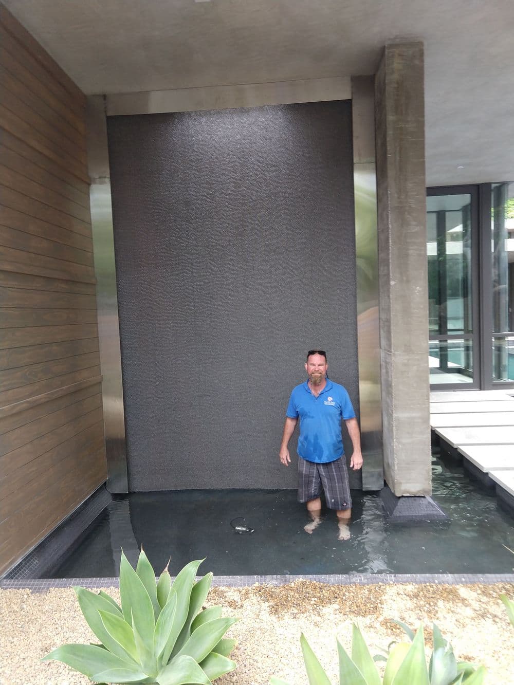Man standing in shallow water in front of a modern water feature at a luxury home.
