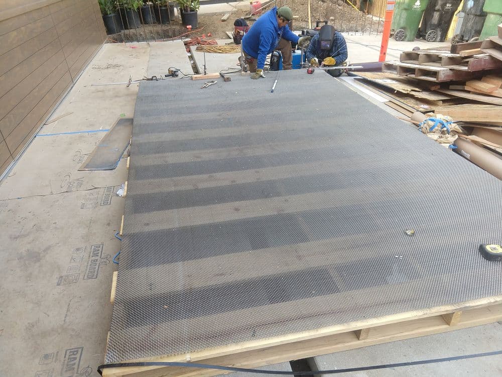 Workers installing a metal grating surface on a wooden platform at a construction site.