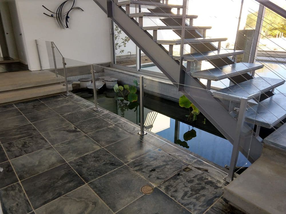 Modern interior with a staircase, glass railing, and a water feature with plants.