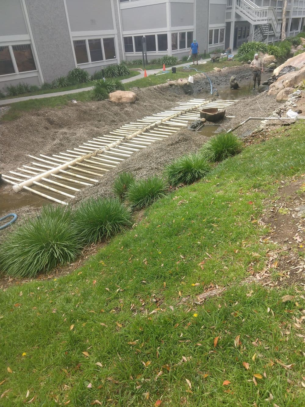 Construction site with workers assembling a gravel landscaping area and wooden framework.
