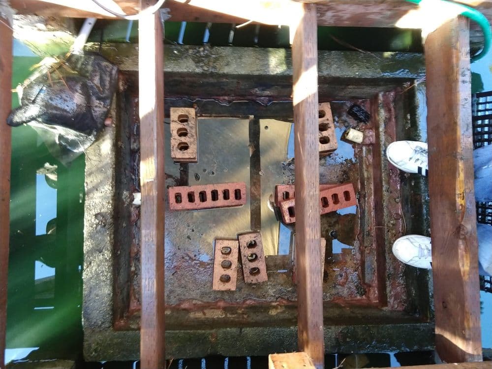 Bird's-eye view of a wooden structure over green water, featuring bricks and a net.