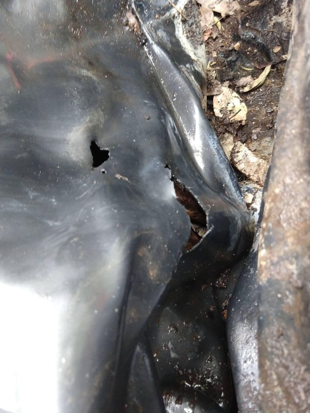 Close-up of damaged black plastic sheeting with tears and dirt in a natural setting.