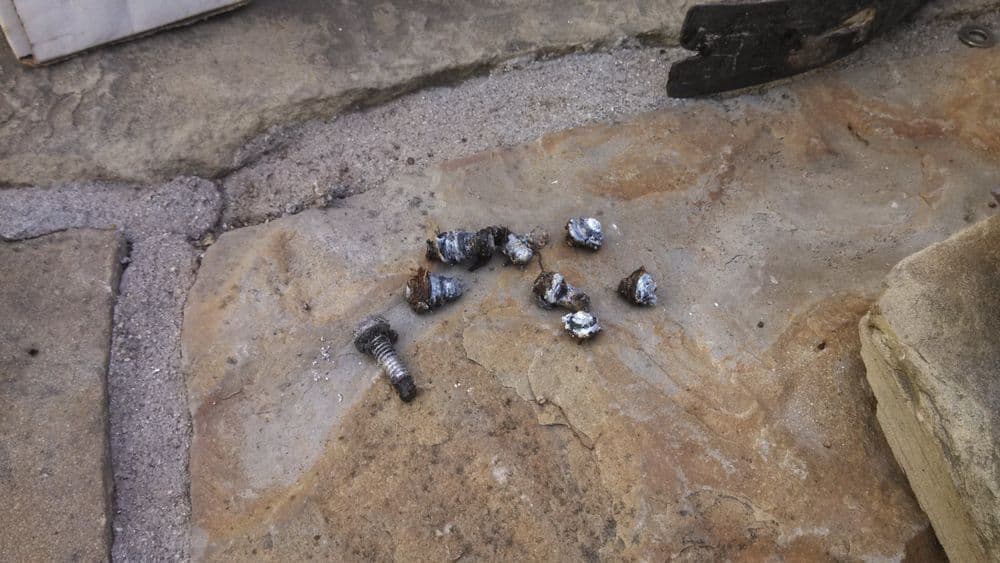 Scattered metal screws and debris on a stone surface outdoors.