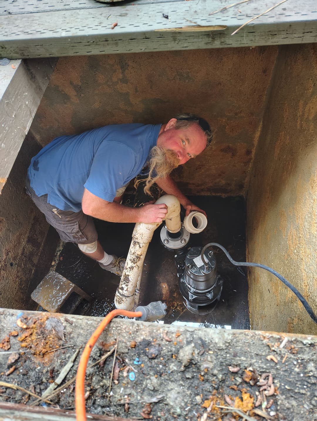 Technician repairing a sump pump in a basement pit, showcasing maintenance work.