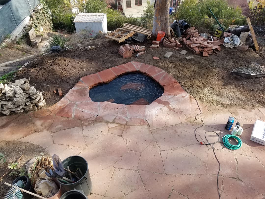 Newly constructed pond surrounded by natural stone, with garden tools and materials nearby.