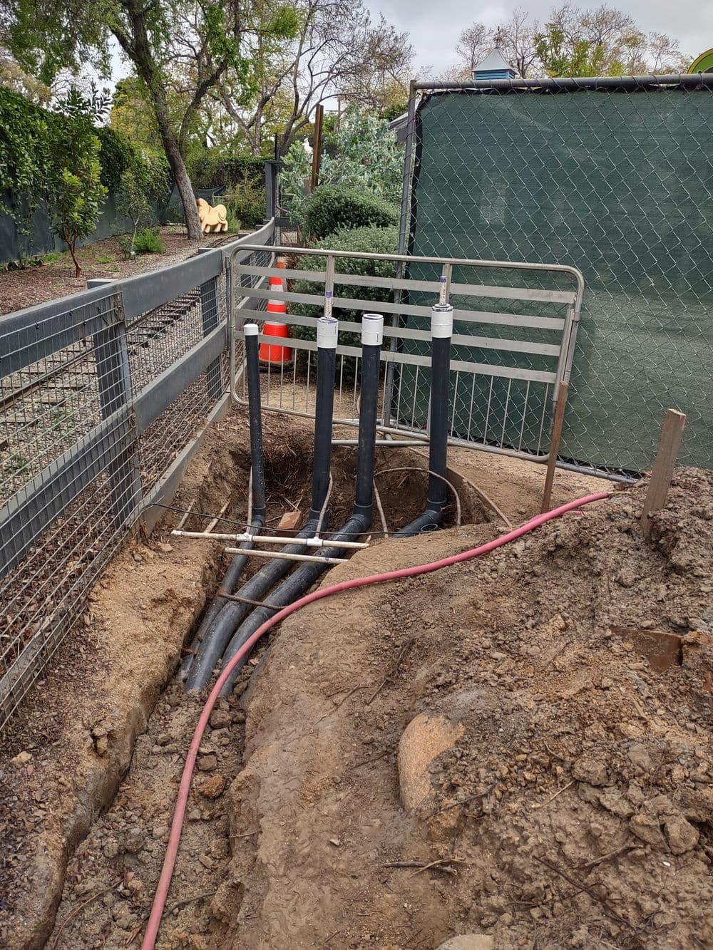 Underground utility pipes with protective fencing and tools at an excavation site.