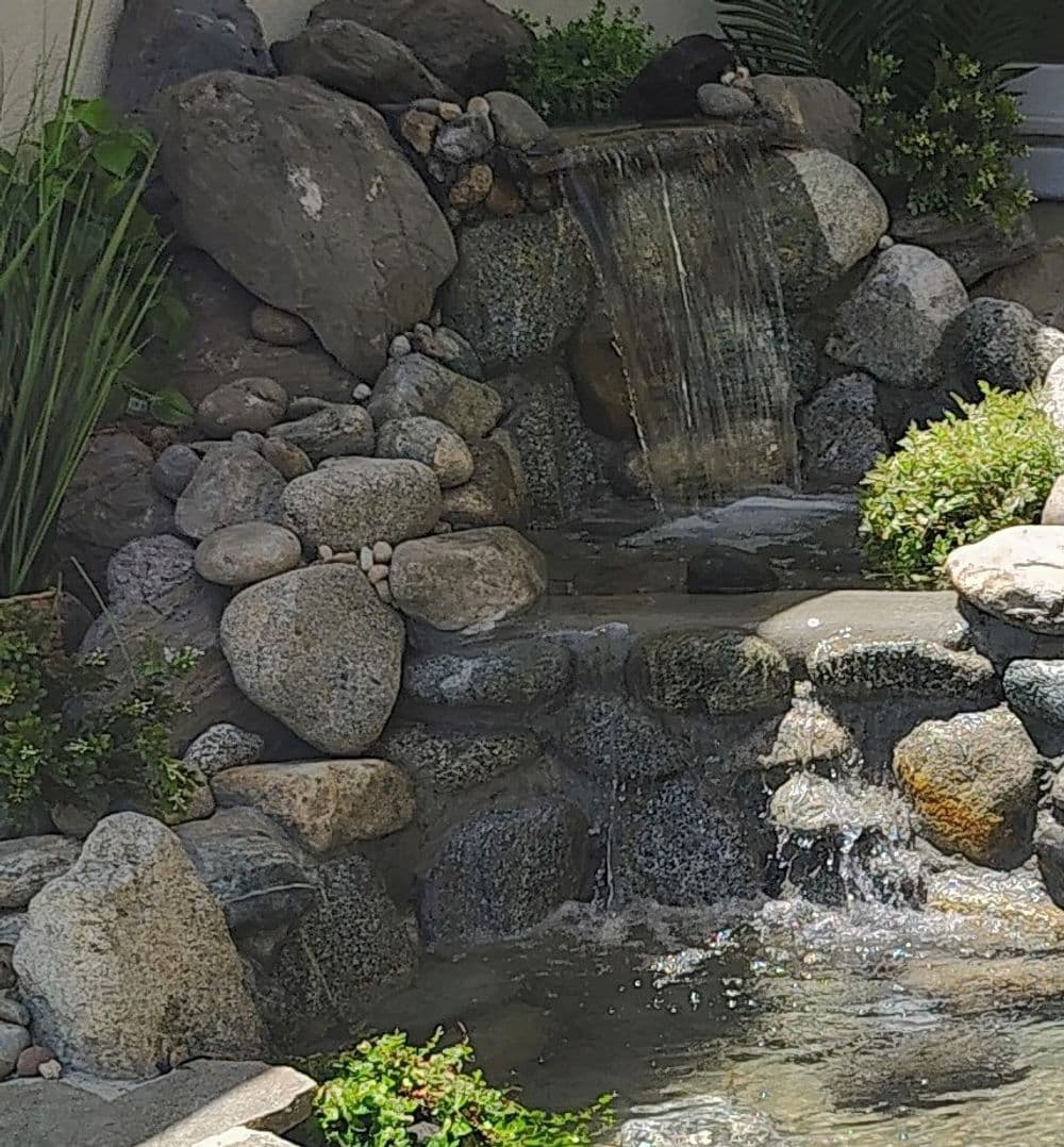 Serene garden waterfall with smooth stones and lush greenery, creating a tranquil ambiance.