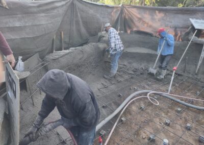 Construction workers pouring concrete at a building site with rebar framework visible.
