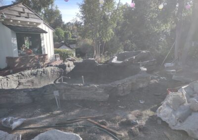 Backyard under renovation with stone landscape, unfinished pool, and construction tools.