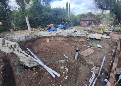 Construction site for a pond featuring rebar, rock formations, and landscaping in progress.