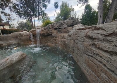 Relaxing rock waterfall feature in a tranquil pool surrounded by lush greenery.