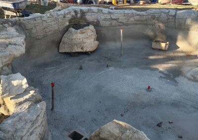 Construction site of a stone-lined pool, showing unfinished concrete and landscaping elements.