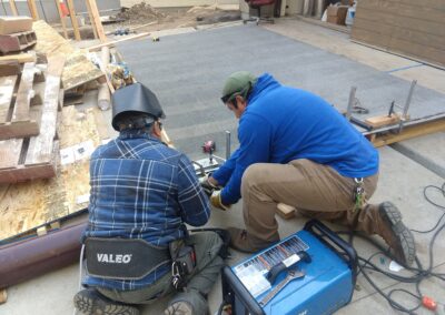 Two workers welding metal components on a construction site with tools and materials around them.