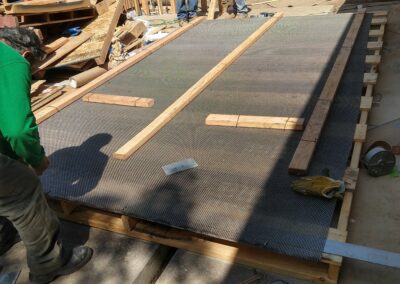 Construction workers installing a mesh foundation on a building site with wooden supports nearby.