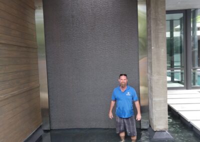 Man standing in shallow water in front of a modern water feature at a luxury home.