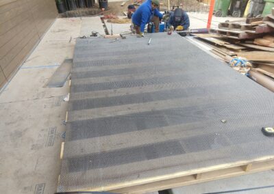 Workers installing a metal grating surface on a wooden platform at a construction site.