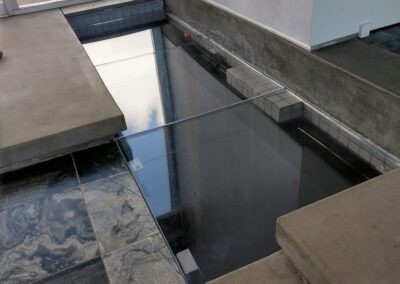 Modern interior featuring a glass floor over a water feature, surrounded by sleek stone tiles.