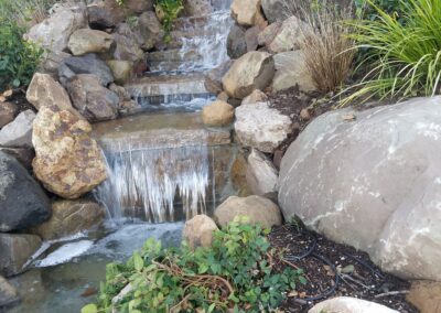 Tranquil waterfall cascading over rocks in a lush, green garden setting.