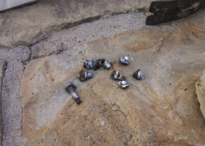 Scattered metal screws and debris on a stone surface outdoors.