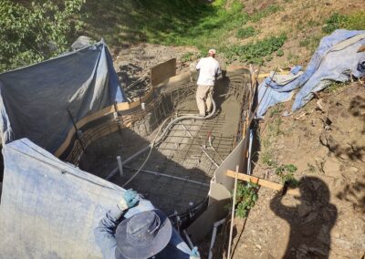 Construction of a concrete pool with workers in a dirt setting, surrounded by protective tarps.