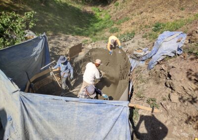 Workers pouring concrete into a foundation form on a construction site surrounded by tarps.