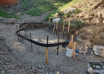 Foundation formwork in a gravel area, surrounded by tools and wooden stakes for construction.