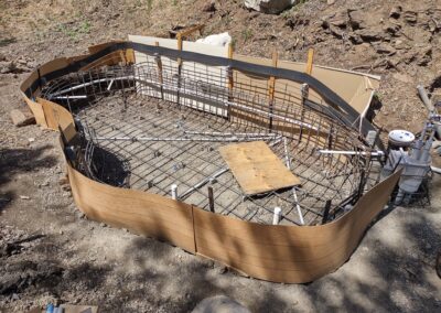 Construction of a curved swimming pool frame with metal rebar and plumbing installed.