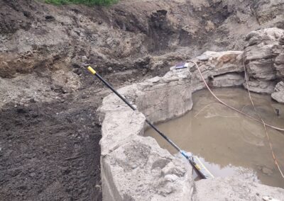 Excavation site with a circular concrete foundation and water-filled pit surrounded by dirt.