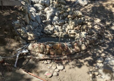 Stone water catchment basin under construction with metal reinforcement and surrounding rocks.