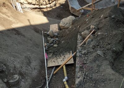 Construction site with excavated earth, gravel, and wooden planks in a rocky area.