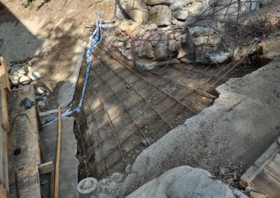 Concrete foundation with rebar grid, rocky surroundings, and construction materials nearby.