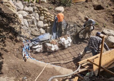 Workers installing rebar and rocks for a landscape structure in a construction site.