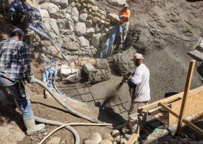 Workers pouring concrete for a stone wall foundation in a construction site.
