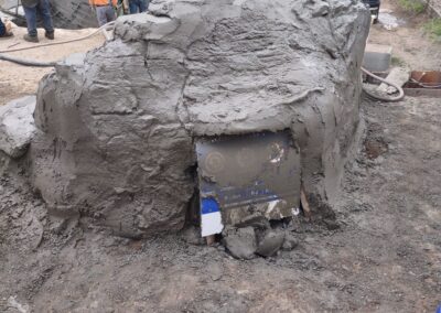 Construction site with workers applying wet concrete to a curved structure. Tools and materials visible.