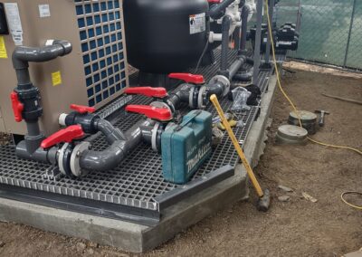 Pump and filtration system with pipes and tools on a gravel base outdoors.
