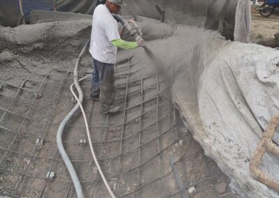 Construction worker spraying concrete over rebar framework at a building site.