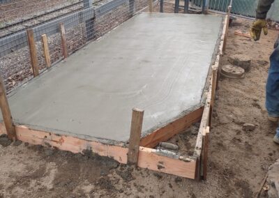 Concrete slab being poured on a wooden frame, outdoors with construction tools nearby.