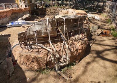 Construction site showcasing a rock formation with reinforcing metal framework and plumbing pipes.