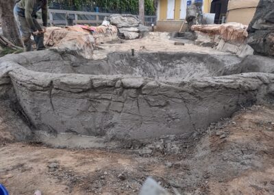 Excavated pond under construction with rough stone edges and tools nearby.