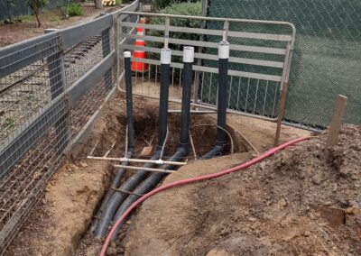 Installation of drainage pipes in a trench surrounded by fencing and landscaping.