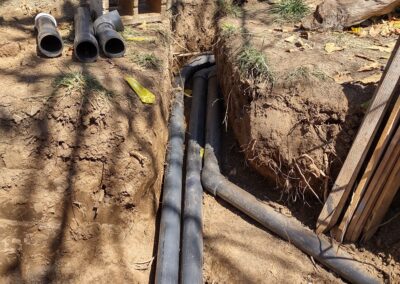 Trenched area with installed black pipes and cinder blocks among dirt and grass.