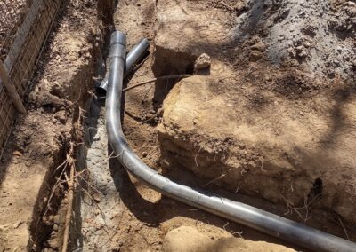 Installation of underground drainage pipes in a trench surrounded by soil and gravel.
