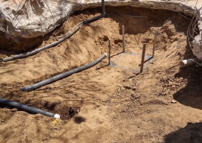 Excavated area with pipes for landscaping project, tools, and rocky surroundings.