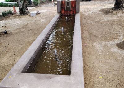 Modern rectangular water feature in a landscaped garden surrounded by trees.